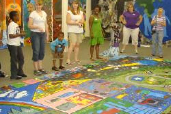 Children standing around a colorful mural that is painted on the floor